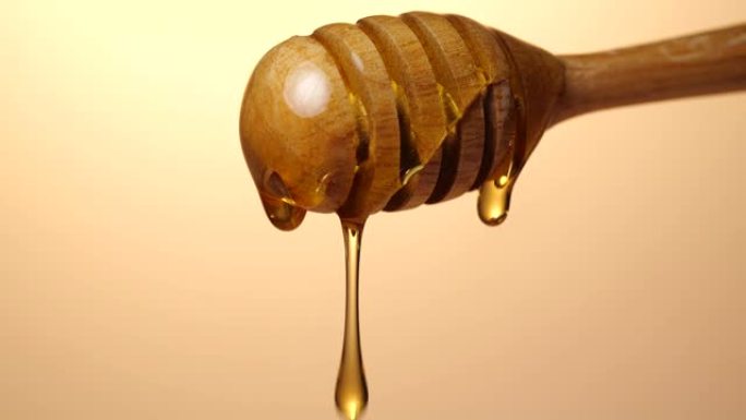 4k分辨率金色背景上的新鲜浓液体蜂蜜从木制铲斗勺中倒出和流出