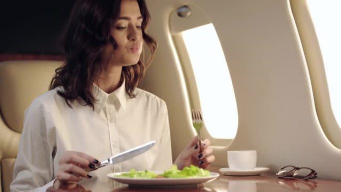 微笑的女商人在乘飞机旅行时吃新鲜沙拉