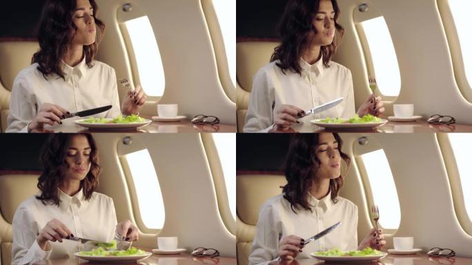 微笑的女商人在乘飞机旅行时吃新鲜沙拉