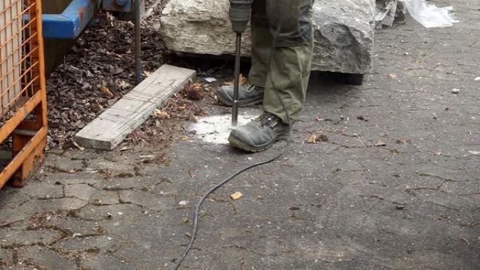 固定安全鞋的工人使用主轴钻头在牢固密封的铺路板上钻穿混凝土块。