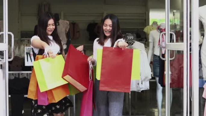 有朋友的亚洲女性拿着购物袋，使用智能手机，在超市/购物中心购物时微笑着