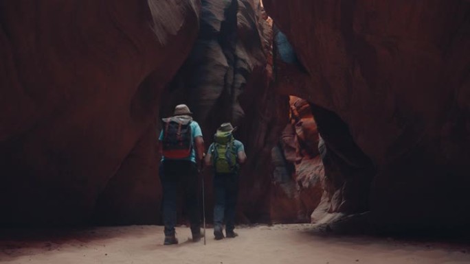 徒步旅行者在带有橙色岩石的深洞槽峡谷中的沙质河床徒步旅行