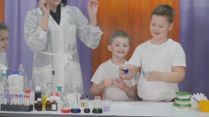 儿童化学实验。儿童有趣的实验。女人用手做魔术动作，蓝色液体变成冰，让孩子们惊讶。房间里充满了人造烟雾