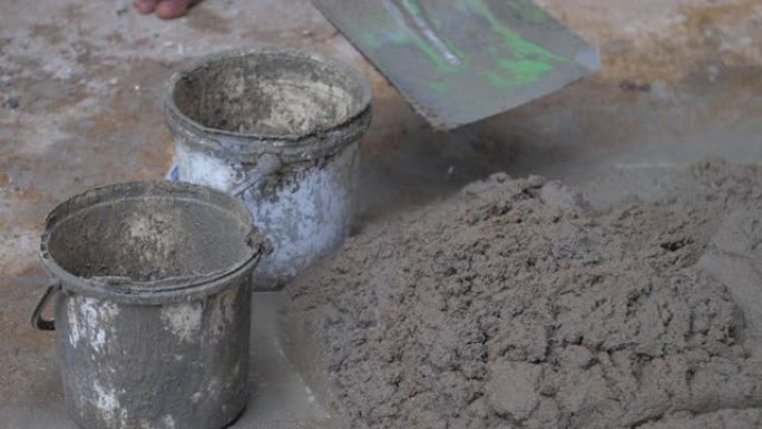 工人用金属铲将湿水泥放入旧桶中