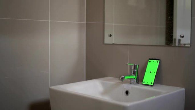 一个年轻人清洁牙齿，看着浴室里的绿屏智能手机