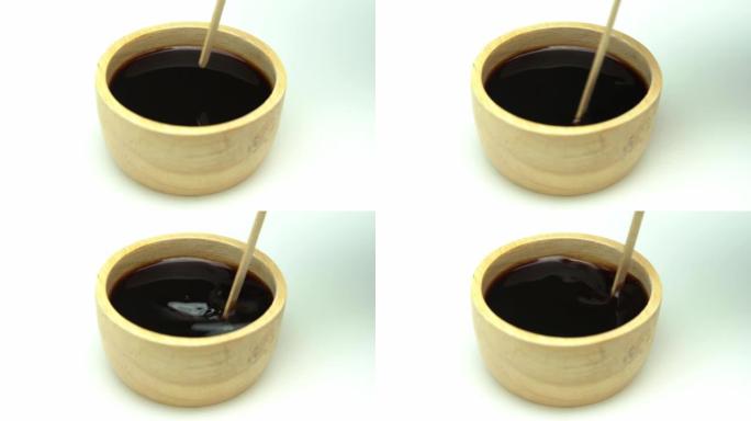 木杯中的黑咖啡和白色背景上的木头制成的咖啡球拍。慢动作。