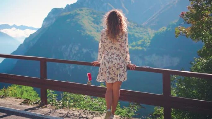 穿着白色碎花印花连衣裙的红色长发的女人在风中飞翔，转身站在桥上享受美丽的俯视图Lago di Gar