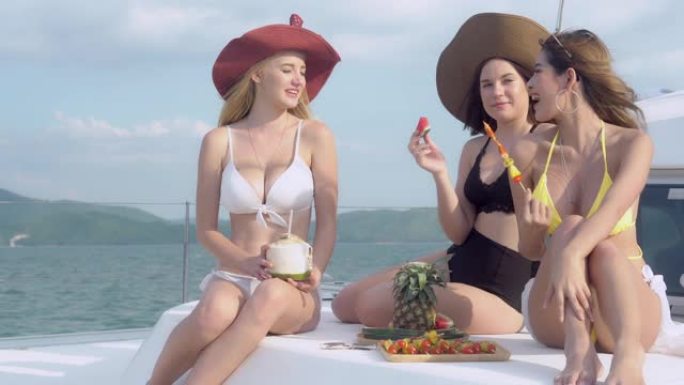 穿着比基尼性感的美丽团体年轻女子一起坐在派对上吃西瓜和烧烤，一起乘船度假，快乐的女孩和朋友一起乘游艇