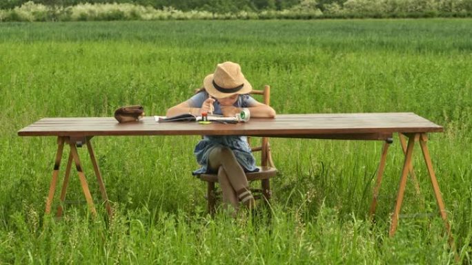 十几岁的女孩坐在田野里的桌子旁做作业。室外视频在线学习