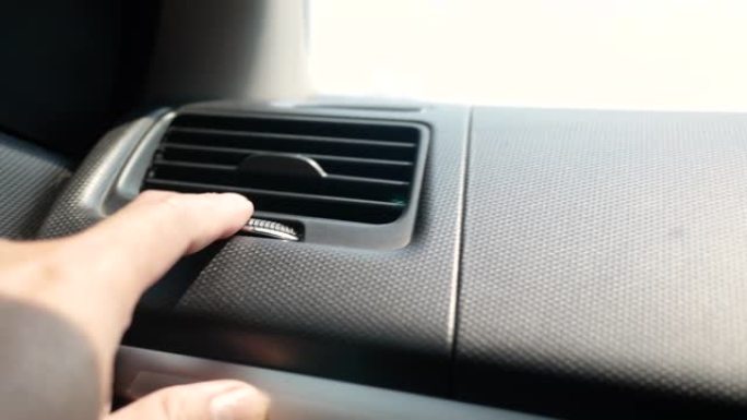 乘客手调节空气通风格栅或调节车内空调按钮的特写。