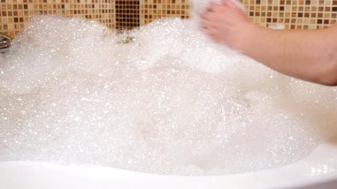 热水浴缸里有很多泡沫。女人的手碰到泡沫
