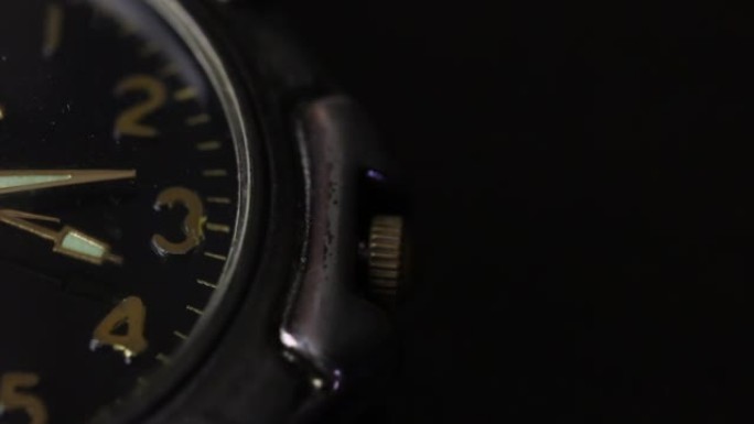 桌子上有一只手表。表盘的一部分是可见的。秒针移动。拍摄特写，在黑色背景上。
