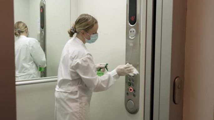 妇女使用湿巾和酒精消毒剂喷雾清洁电梯按钮控制面板。消毒，清洁和保健，抗冠状病毒新型冠状病毒肺炎