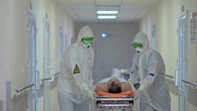穿着防护服的医生在医院走廊的担架上抬病人。冠状病毒感染者的住院治疗。病人被带在担架上。