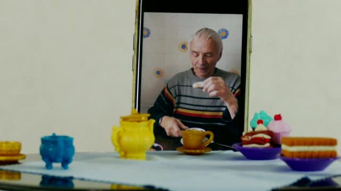 智能手机中的老人在娃娃桌上喝茶