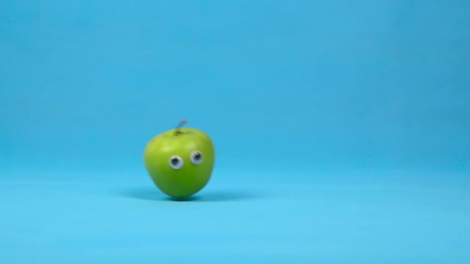 眼睛慢慢滚动的青苹果。蓝色背景上有卷的苹果。慢动作。