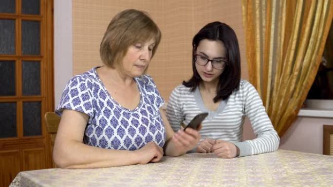 女儿教妈妈如何使用电话。一名年轻女子向她的老母亲展示了在哪里点击智能手机。那个女人打了电话。一家人坐
