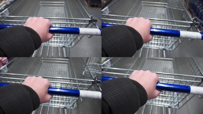 男性手握着购物车的把手在商店的瓷砖上滚动。第一人称视角特写。