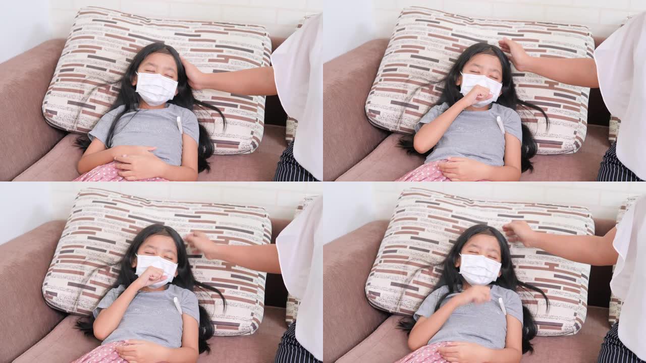 亚洲小女孩戴着外科口罩，躺在咳嗽的沙发上。妇女使用儿童温度计。