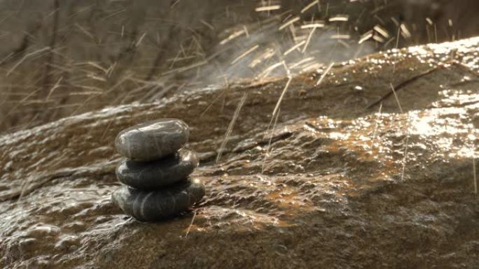 在阳光下飞溅瀑布的背景下，一堆石头在潮湿的表面上平衡