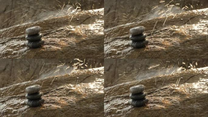 在阳光下飞溅瀑布的背景下，一堆石头在潮湿的表面上平衡