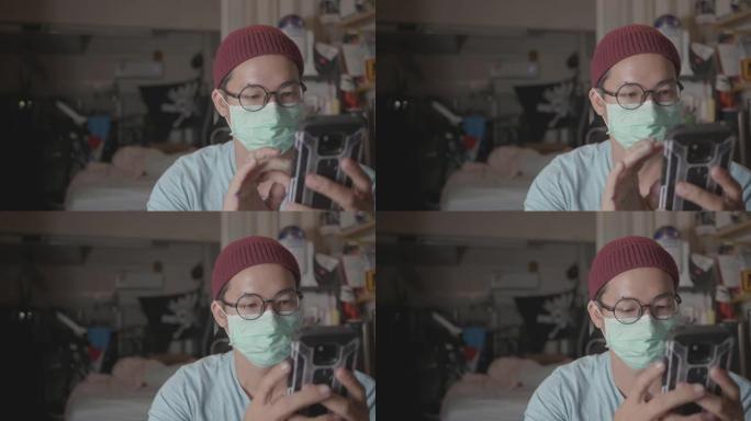 亚洲男性在检疫期间使用智能手机佩戴医用口罩。新型冠状病毒肺炎在家。
