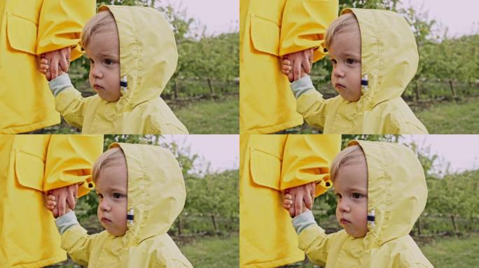 穿着黄色雨衣的可爱男婴肖像。孩子握着妈妈的手。爱，关怀，依恋，家庭，孩子概念。