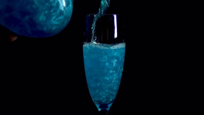 将蓝色饮料倒入黑色背景上的玻璃杯中。长生不老药旋转闪烁。爱情的药水被隔离在黑色背景上。