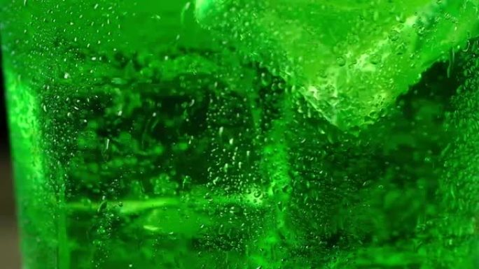 冷冰块漂浮在绿色的碳酸鸡尾酒中旋转。