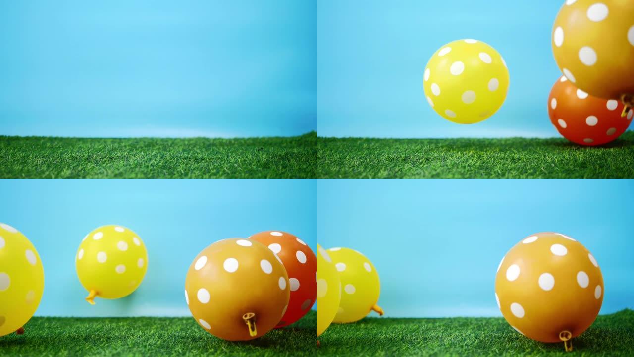 黄色和橙色的气球落在绿色的草地上，慢动作。