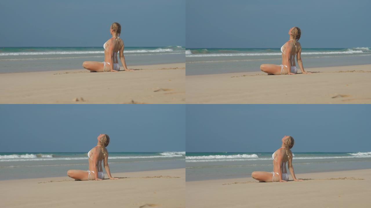 女士弯曲的膝盖坐在沙滩上，看着晴朗的天空