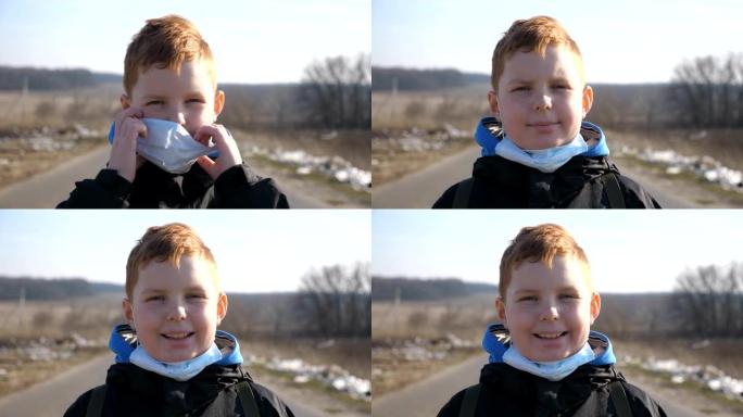 站在户外的戴着医用口罩的小男孩的肖像。快乐的男孩子从病毒和微笑中脱下防护面具。冠状病毒和流行病的健康