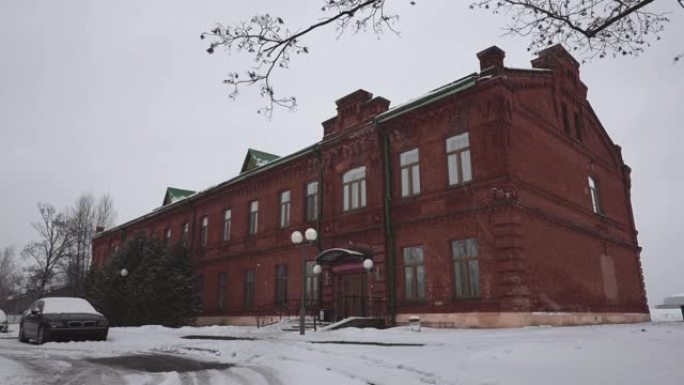 旧红砖建筑前兵营18 19世纪冬天白天下雪。俄罗斯帝国最古老的旅馆或旅舍时代的游客正在缓慢地遭遇暴风