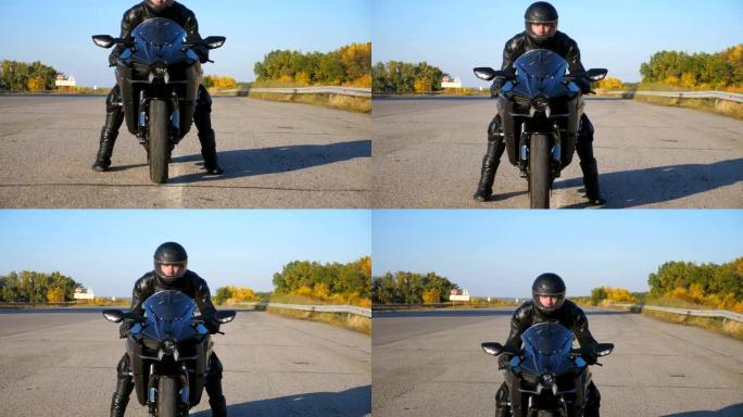 戴着头盔和皮夹克的年轻骑自行车的人正坐在高速公路上的摩托车上，准备骑车。男人要骑运动摩托车。自由和冒
