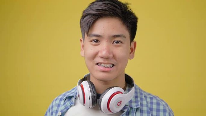 黄色背景上戴着耳机的快乐亚洲少年男孩。