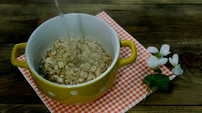 素食健康早餐加粥。黄碗中的燕麦片片倒入水。