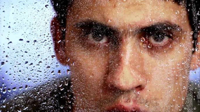 雨后，盖伊·高加索人的外表透过潮湿的窗户看。特写。