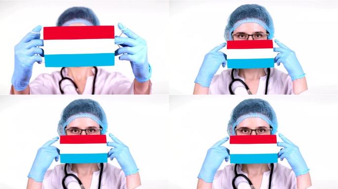 特写。戴眼镜的医生，蓝色医疗帽，手套手持带有卢森堡国旗的医用口罩。医生护理，冠状病毒期间国家保护，全
