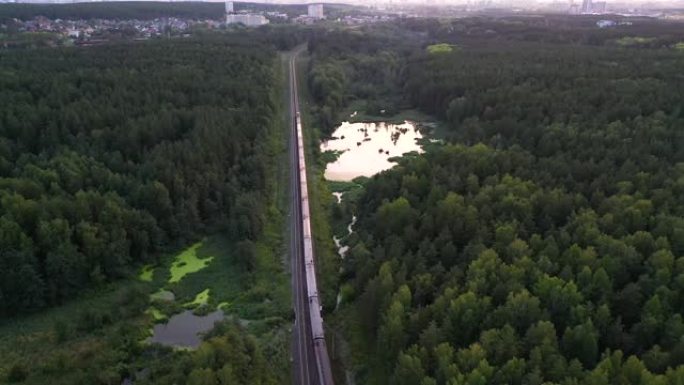 在俄罗斯卡累利阿的湖泊和森林中的双线铁路上，货运列车的车厢经过一段距离。鸟瞰图