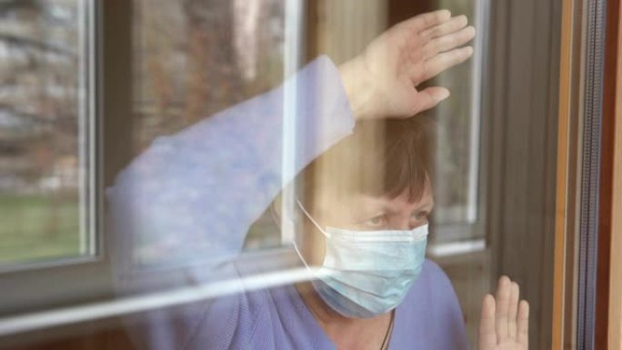 一位戴着医用口罩的老妇看着窗外。检疫自我隔离，冠状病毒，covid 19。
