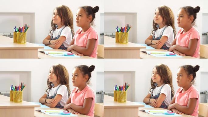 两个女学生坐在教室里的桌子上，仔细听老师的话