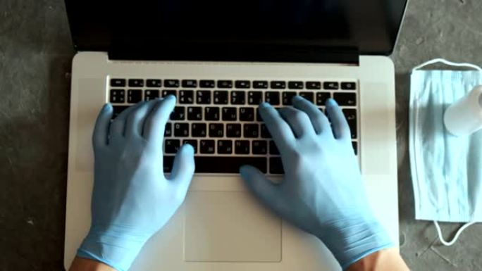 年轻的商人戴着医用口罩手套，坐在家庭办公室的笔记本电脑上工作。在冠状病毒covid 19检疫概念上做