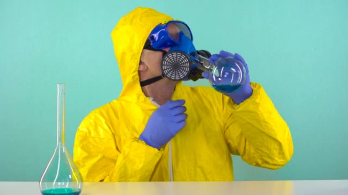 一名穿着黄色防护服，戴着手套和眼镜的化学技术人员正试图通过防护口罩从烧瓶中饮用蓝色化学液体。化学、微