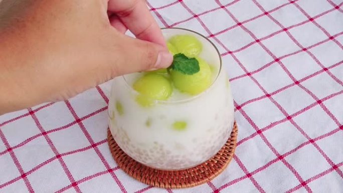 自制甜西米酱配椰奶、泰国甜点甜瓜球和女人手，将薄荷放在上面。泰国菜。