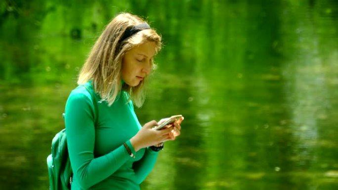 拥有智能手机的年轻女子在森林河流的背景下