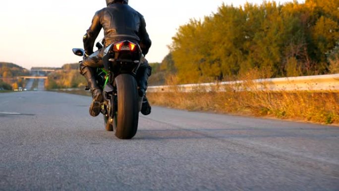 无法识别的戴头盔的人在高速公路上快速骑现代运动摩托车。摩托车手在乡间小路上骑摩托车。旅途中开车的人。