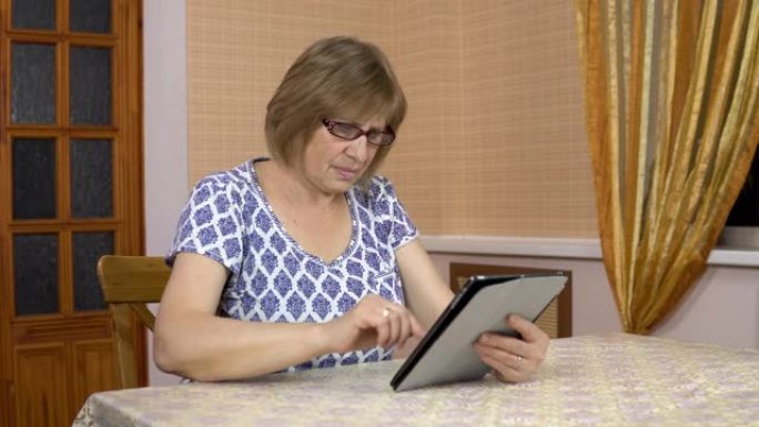 一个女人第一次使用平板电脑。老妇人不明白如何使用平板电脑，戳她的手指，然后把它放下。舒适房间里的女人