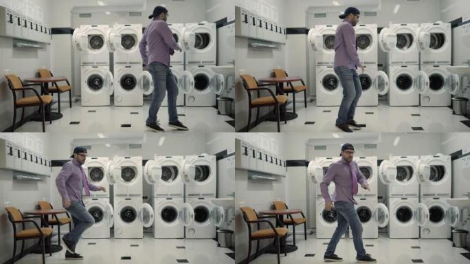 快乐的男人戴着帽子，戴着眼镜，在洗衣房里欢快地跳舞。男子跳病毒舞，在洗衣房玩得开心。快乐的家伙喜欢跳
