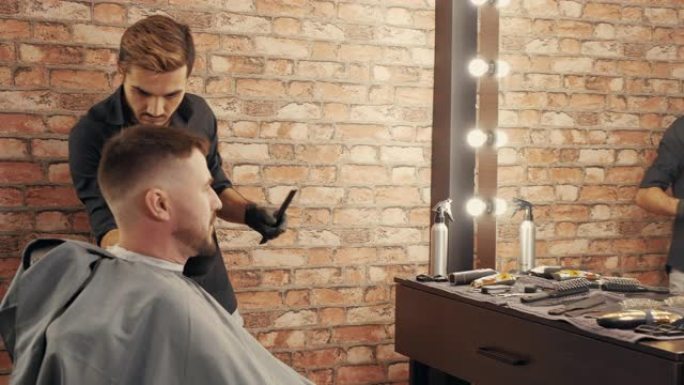 理发师在沙龙剃须和理发后从男性脸上扫除胡茬。男理发师在理发店为大胡子客户服务。沙龙中的男性头发和胡须