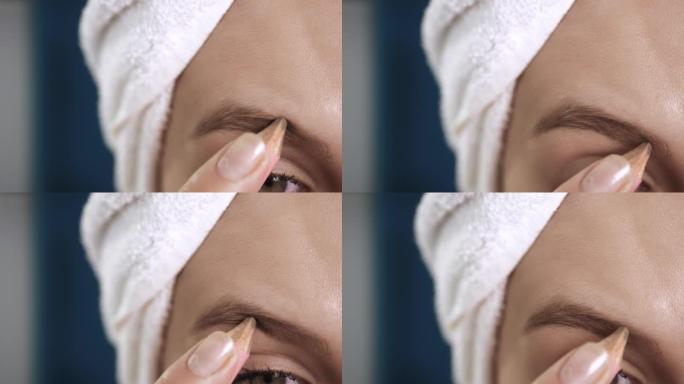 女孩画眉毛。微距拍摄的脸有吸引力的女人与毛巾在蓝色的背景油漆眉毛与特殊的铅笔。化妆师，美容，洁面，化